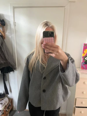 Grå oversized kappa med knappar - Säljer en grå oversized kappa med två stora svarta knappar framtill. Kappan har en rak och boxig passform med breda ärmar och enkel krage. Perfekt för hösten