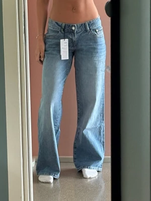 Ljusblåa vida jeans med hög midja - Säljer ett par ljusblå jeans med breda ben och hög midja. Jeansen har klassisk femficksdesign och stängs med knapp och dragkedja. Perfekta för en avslappnad och trendig look. Materialet är denim i bomull.