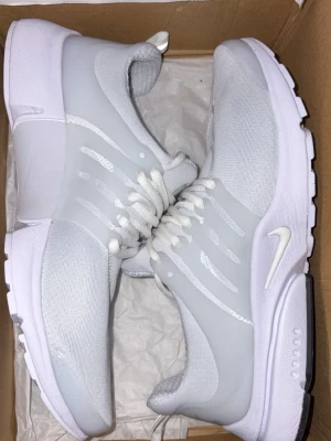 Nike vita Air sneakers - Snygga vita Nike Air sneakers med mesh- och syntetmaterial för en clean look. Skorna har vita snören, diskret Nike-logga på sidan och AIR-detalj bak. Perfekta för dig som gillar stilrena och sportiga sneakers.