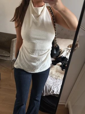 Vit halterneck topp med öppen rygg - Säljer en snygg vit halterneck topp med öppen rygg och knytband. Toppen har en draperad framsida och är gjord i ett mjukt, stretchigt material som sitter skönt på kroppen. Perfekt för dig som vill ha en trendig och stilren look. Aldrig använd.💕