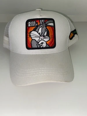 Vit keps med Bugs Bunny-motiv - Snygg vit keps med broderad Bugs Bunny på framsidan och mesh på sidorna för extra ventilation. Kepsen har böjd skärm och justerbar snapback baktill. Perfekt för dig som gillar Looney Tunes och vill sticka ut med en unik accessoar.