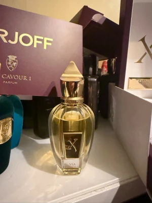 Xerjoff Via Cavour 1 Parfym - Lyxig parfym från Xerjoff i elegant glasflaska med gulddetaljer och spetsigt lock. Flaskan har en exklusiv design med en guldig etikett och levereras i en stilren lila och vit presentask. Doften är unisex och flaskan utstrålar premiumkänsla. Mängd kvar finns på bilden