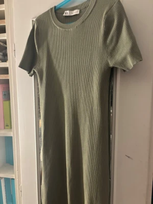 Ribbad grön klänning från Zara - Snygg ribbad klänning från Zara i en mjuk olivgrön nyans. Modellen har korta ärmar, rund halsringning och är figurnära med stretchigt material. Perfekt för dig som gillar enkel men trendig stil.