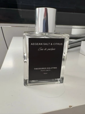 Aegean Salt & Citrus Eau de Parfum - Fräsch parfym med doft av Aegean Salt & Citrus från Theodoros Kalotinis. Flaskan är rektangulär i genomskinligt glas med en stilren svart etikett och silverfärgad kork. Innehåller 50 ml Eau de Parfum som ger en fräsch och citrusaktig känsla.