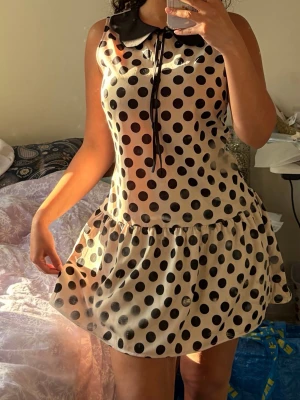 Polkadott klänning/ Prickig kort klänning med krage - Supersöt trendig polkadott kort klänning i beige med stora svarta prickar. Klänningen är ärmlös, har en svart krage med knytband och en volang nedtill. Säljer den billigt då den har fläckar som troligen går att fixa☺️Strl står ej men antar S/XS då den passar mig som är Xs. 