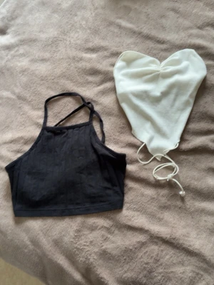 Svart ribbad croppad linnetopp & vit tubtopp - Säljer två toppar: en svart ribbad croppad linnetopp med tunna axelband och en vit tubtopp i bandeau-modell med snörning. Perfekta för sommaren. Storlek Xs men passar även Xxs. 
