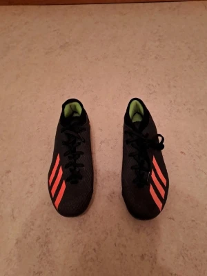 Svarta Adidas fotbollsskor med röda detaljer - Säljer ett par svarta Adidas fotbollsskor med röda ränder och detaljer. Skorna har snörning, mönstrad ovandel och grönt foder. Yttersulan har röda dobbar för bra grepp på planen. Perfekta för dig som vill sticka ut på matchen! I mycket bra skick. Säljs för 200 kr. Tveka inte att kontakta om du är intresserad eller har några frågor! Först till kvarn dom gäller!