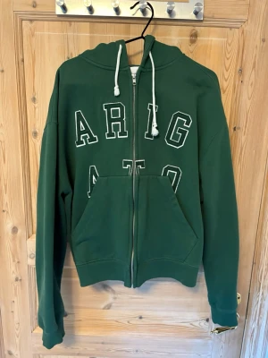Grön hoodie från Axel Arigato - Mörkgrön zip up hoodie från Axel arigato i 100% bomull. Perfekt för streetwear look. Nypris 2090 kr. Knappt använd.