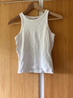 Vit ribbad linnetopp - Säljer en enkel och stilren vit ribbad linnetopp med rund halsringning och ärmlös design. Perfekt att matcha med jeans eller kjol för en clean look. Materialet känns mjukt och stretchigt, vilket gör toppen bekväm att bära hela dagen.