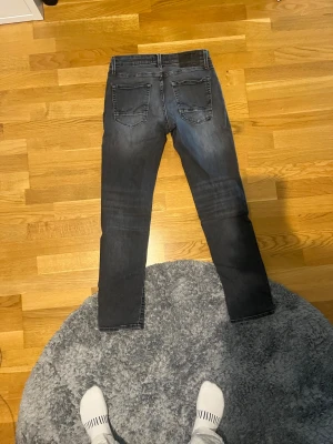 Jack and Jones slim Glenn  - Säljer ett par mörkgrå slim fit jeans med snygga slitningar och klassisk femficksdesign. I modellen slim Glenn. Jeansen har en något tvättad look och snygg slitningar vid fickorna raka. Perfekta för dig som gillar en stilren men avslappnad vibe.