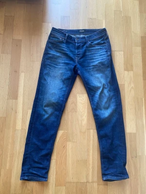 Blå tapered jeans från Jack & Jones - Snygga blå jeans från Jack & Jones i modellen Tapered/Mike. Jeansen har klassisk femficksdesign, normalhög midja och avsmalnande ben. Tillverkade i slitstarkt denim med snygga tvättade detaljer och kontrastsömmar.