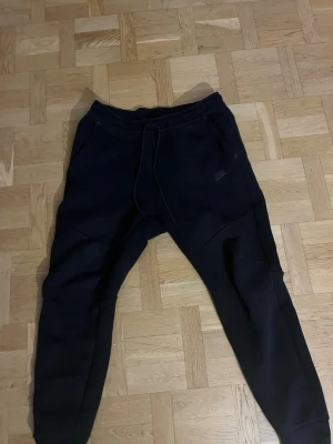 Nike tech svarta byxor  - Säljer ett par svarta mjukisbyxor nike. Byxorna har en avslappnad passform och synliga sömmar framtill. Perfekta för chill dagar eller träning.