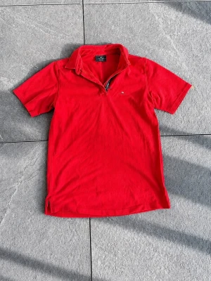 Röd kortärmad polotopp med dragkedja - Snygg röd polotopp från Bygelert med korta ärmar och dragkedja framtill. Klassisk krage och diskret logga på bröstet. Perfekt för dig som gillar sportig stil och vill sticka ut med färg.