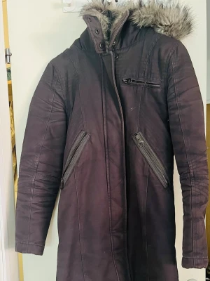 Vintage TopShop svart vinter jacka - Säljer en lång, antracit grå parkas med fuskpäls på huvan. Jackan har tre dragkedjefickor framtill och quiltad insida med tryckt text. Perfekt för kalla dagar och har en hög krage för extra värme. Stängs med dragkedja och tryckknappar.