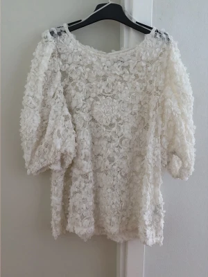 Vit spetsblus från Holly & Whyte - Superfin vit blus från Holly & Whyte med 3D-blommig spets och rund halsringning. Blusen har trekvartsärm och en luftig, romantisk look. Perfekt för dig som vill ha något extra till din outfit.