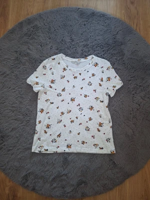 Vit blommig t-shirt från Clockhouse - Säljer en vit t-shirt från Clockhouse med små blommiga tryck i orange, gul och svart samt diskreta prickar. T-shirten har korta ärmar och är gjord i mjuk bomull, perfekt för en avslappnad och trendig look.
