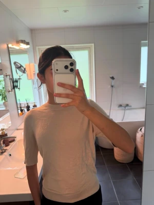 Beige kortärmad stickad t shirt - Snygg beige stickad tröja med korta ärmar och rund hals. Tröjan har en enkel och stilren design som passar perfekt till jeans eller kjol. Materialet ser mjukt och bekvämt ut, och modellen är något figurnära.