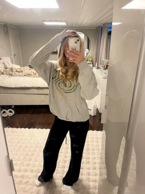 Grå hoodie med tryck och huva - Säljer en grå hoodie med stort grafiskt tryck i grönt och gult på bröstet. Hoodien har en klassisk huva och ribbade muddar vid ärmslut och nederkant. Perfekt för en avslappnad och chill stil.
