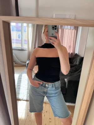 Svart tubtopp med öppen rygg - Säljer en svart tubtopp med unik halsringning och öppen rygg. Toppen är tight och croppad, perfekt för dig som vill ha en trendig och stilren look. Materialet känns mjukt och stretchigt. Aldrig använd, endast testad och tvättad
