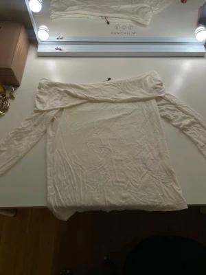 Off shoulder topp från 157, vit - Säljer en vit off shoulder topp från 157 i storlek XS. Toppen har långa ärmar och en bred, nedvikt krage som ger en snygg och avslappnad look. Tillverkad i mjukt och stretchigt material som sitter skönt på kroppen. Perfekt till jeans eller kjol.
