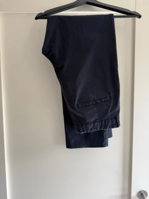 Mörkblå chinos med rak passform - Snygga mörkblå chinos med rak passform och klassiska fickor bak. Tillverkade i ett mjukt och bekvämt bomullsmaterial som ger en stilren look. Perfekta för dig som vill ha ett par stilrena byxor till garderoben.