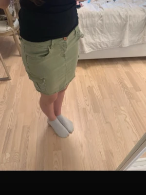 Grön kortkjol med fickor - Snygg grön kortkjol med stora sidofickor och knappstängning i midjan. Kjolen har en avslappnad passform och är perfekt för dig som gillar en enkel men cool stil. Passar till både t-shirt och hoodie för en casual look.