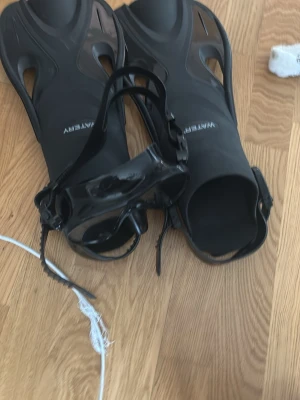 Svart snorkelset med fenor och mask bundle paket  - Säljer ett svart snorkelset från Watery med ett par fenor och en matchande dykmask. Fenorna är i plast och masken har silikonband och klart tempered glas. Perfekt för snorkling eller simning i havet.