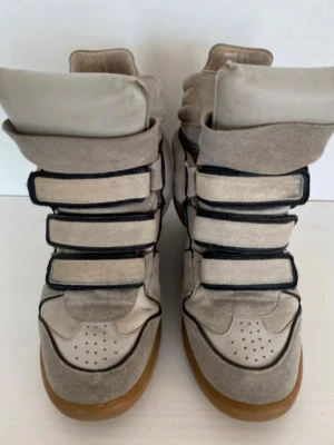 Isabel Marant skor - Snygga höga Isabel  Marant sneakers i beige mocka och textil med flera breda kardborreband och kontrasterande svarta detaljer. Skorna har perforerad tå och brun sula som ger en retrovibe. Perfekta för dig som vill sticka ut med en unik och sportig look.
