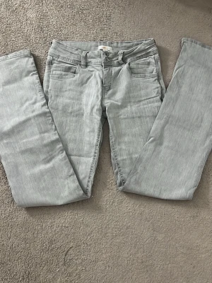 Gina Tricot Ljusgrå raka jeans  - Säljer ett par ljusgrå jeans med rak passform och är low waist. Jeansen har bälteshällor, knappgylf och är tillverkade i ett mjukt denimtyg. Perfekta för en clean och stilren look. 