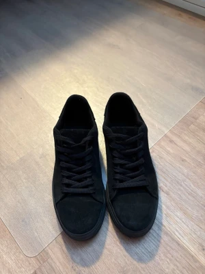 Helvita svarta sneakers i mocka - Snygga helsvarta sneakers med låg profil och klassisk design. Skorna har ovandel i mocka och matchande svarta skosnören samt sula. Perfekta för dig som gillar en clean och stilren look till vardagsoutfiten.