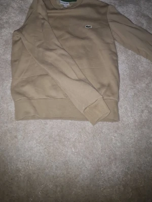 lacoste tröja herr som ny användare typ 2gånger och är äkta - Snygg beige sweatshirt från Lacoste i klassisk modell med rund hals och broderad krokodil-logga på bröstet. Tröjan har ribbade muddar vid ärmslut och nederkant. Perfekt för en chill och stilren look.
