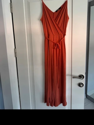 Rostfärgad jumpsuit från Bik Bok - Säljer en snygg rostfärgad dräkt från Bik Bok med smala axelband, omlott upptill och knytband i midjan. Dräkten är i ett mjukt, stretchigt tyg som faller fint och har en avslappnad men ändå elegant look.