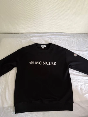 Moncler set - Två snygga tröjor från Moncler. En svart sweatshirt med vit Moncler-logga på bröstet och patch på ärmen, samt en svart långärmad piké med krage och Moncler-märke på bröstet. Båda har detaljer i rött, vitt och blått. Perfekta för en stilren look.