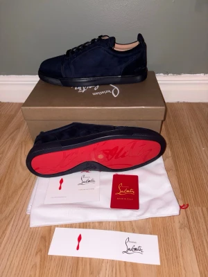 Christian Louboutin Mörkblå Mockasneakers – Lyx & Stil - Snygga mörkblå sneakers i mocka från Christian Louboutin med den ikoniska röda sulan och broderad logga på hälen. Skorna har lågt skaft, svarta skosnören och en stilren design som sticker ut. Perfekta för dig som vill ha något exklusivt och trendigt.