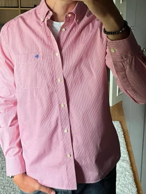 Morris skjorta i röd/vitrandig - stl 42 (L) - 100% bomull, rak passform med button down rage och bröstficka med blått märke. Tunn och lätt, funkar bra på sommaren till jeans eller vita byxor. Personen på bilden är 189cm, väger 78kg.  Använd men i mycket fint skick, inga hål eller fläckar.  Rök- och djurfritt hem. Skriv gärna om du vill ha fler bilder eller undrar något!