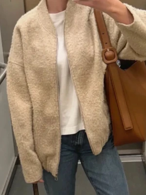 Beige teddyjacka från Zara - Mysig beige teddyjacka från Zara med dragkedja framtill och avslappnad passform. Jackan har ribbade muddar vid ärmslut och nederkant samt två sidofickor. Perfekt för lager på lager och ger en trendig look till jeans eller kjol.