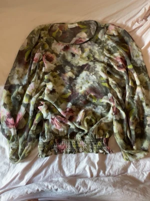Blommig blus från STOCKH LM - Säljer en transparent blommig blus från STOCKH LM i storlek 36. Blusen har långa ärmar, resår i midjan och ett romantiskt blommönster i grönt, rosa och vitt. Perfekt för dig som vill ha en luftig och trendig topp med unik look.