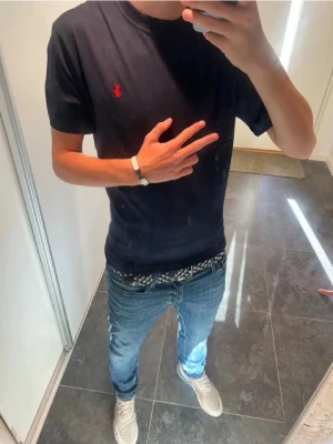 Mörkblå t-shirt från Ralph Lauren - Snygg mörkblå t-shirt från Ralph Lauren med den klassiska röda loggan broderad på bröstet. T-shirten har normal passform och korta ärmar. Perfekt till jeans eller shorts för en clean och stilren look.