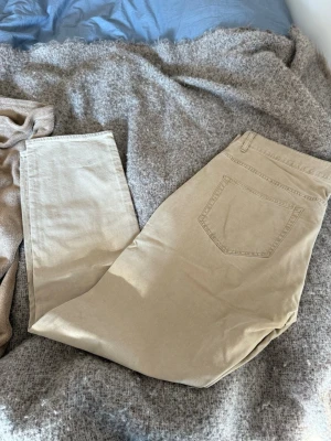 Beige jeans med rak passform - Snygga beige chinos med klassisk rak passform och bakficka. Tillverkade i mjukt bomullstyg som känns skönt mot huden. Perfekta för dig som gillar en clean och enkel stil. Passar till det mesta och är lätta att matcha med olika plagg.