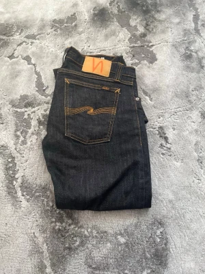 Mörkblå jeans från Nudie Jeans - Stolek w30 L34 modell super slim kim Säljer ett par mörkblå jeans från Nudie Jeans med klassisk femficksmodell och kontrastsömmar i gult. Jeansen har rak passform och är tillverkade i kraftigt denimtyg. Perfekta för dig som gillar stilrena och tidlösa jeans.