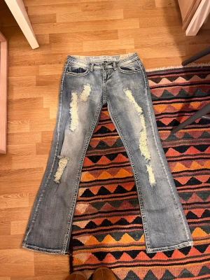 Bootcut slitna jeans Vanilla Star - Säljer ett par blå bootcut jeans från Vanilla Star med slitna detaljer och råa kanter på benen. Jeansen har klassisk femficksmodell och ljus tvätt med tydliga slitningar framtill. Köpte dom i USA i en vintage second hand butik för ca 1000kr. Skicket är basically helt nytt då dom aldrig kommit till användning. Skulle säga att storleken är 40/42.