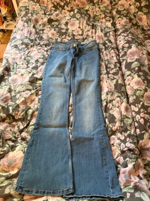 Blå utsvängda jeans med hög midja - Säljer ett par blå jeans med utsvängda ben och hög midja. Klassisk femficksmodell med knapp och dragkedja framtill. Jeansen har en snygg tvätt och är perfekta för dig som gillar retrostil. Materialet är denim i bomull.