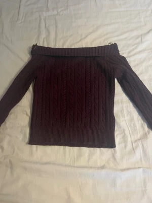Vinröd off shoulder stickad tröja - Säljer en vinröd stickad tröja som aldrig är använd  från Gina Tricot med off shoulder-design och kabelstickat mönster. Tröjan har långa ärmar och bred ribbad kant upptill och nedtill. Perfekt för dig som vill ha en trendig och mysig look. Passar xs/s 