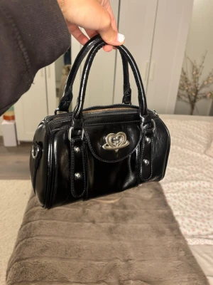 Svart handväska - Snygg svart handväska med supersöt detalj framtill⭐️Finns ett längre band till också som man kan ta på och av (se bild 5) 💕