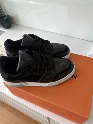 Louis Vuitton skor 43 - Louis Vuitton sneakers i svart med monogrammönster och vita sulor. Skorna har låga skaft, svarta skosnören och detaljer i läder. Kommer med originalkartong och dustbags. Perfekta för dig som vill ha en exklusiv och stilren look. De är storlek 42 men passar 43