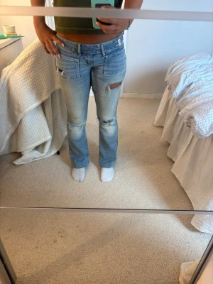 Ljusblå slitna jeans Gina Tricot - Ljusblå jeans från Gina Tricot med slitningar och hål på låret och knät. Modellen har låg midja, raka ben och klassiska fem fickor. Jeansen har en tvättad look och är tillverkade i denim med lite stretch för skön passform.