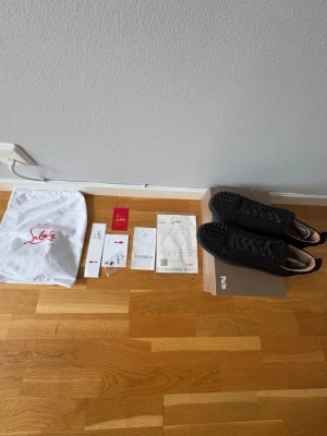 Svarta spikes-sneakers Louboutin - Säljer ett par svarta sneakers från Christian Louboutin med ikoniska svarta spikes över hela tån och sidan. Skorna är låga, har snörning och är tillverkade i mocka med gummisula. Medföljer originalpåse, box och äkthetskort.