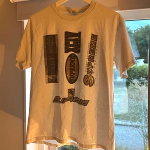 Supreme multi logos t-shirt fw21 - Säljer en vit/krämvit supreme t-shirt från fw21 kollektionen. T-shirten har flera bruna Supreme-loggor tryckta framtill i olika stilar och storlekar. Klassisk passform och rund hals. Sparsamt använd!