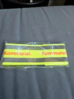 Reflexband med tryck Kommunal - Snyggt neongult reflexband med grå reflexränder och röd texten 'Kommunal.' Perfekt för att synas i mörkret. Tillverkat i elastiskt material och passar att ha runt armen eller benet.