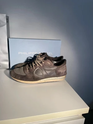 Gråa Philippe Model Trainers Sneakers - Ett par snygga Philipe model trainers. Det finns lite slitningar på toppen av skon men inget som är väldigt synligt. Sulan är lite mer sliten.🙂                       Var snäll och notera att bilderna inte är så bra och skorna är väldigt smutsiga. Jag kan rengöra och skicka nya bilder vid eventuellt köp. Priset är inte huget i sten👍 Sko lådan får man även med med köp